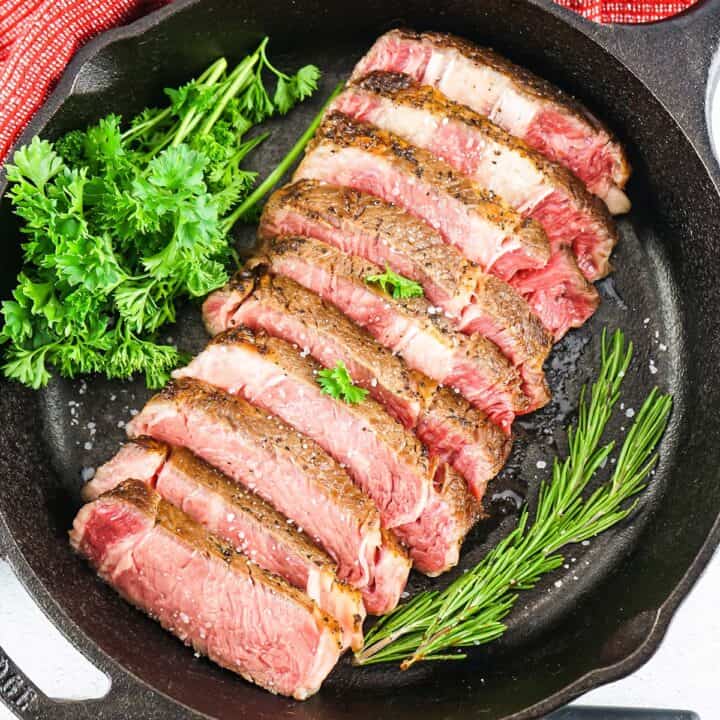 sous vide ribeye steak sliced in a cast iron pan with fresh herbs in the pan