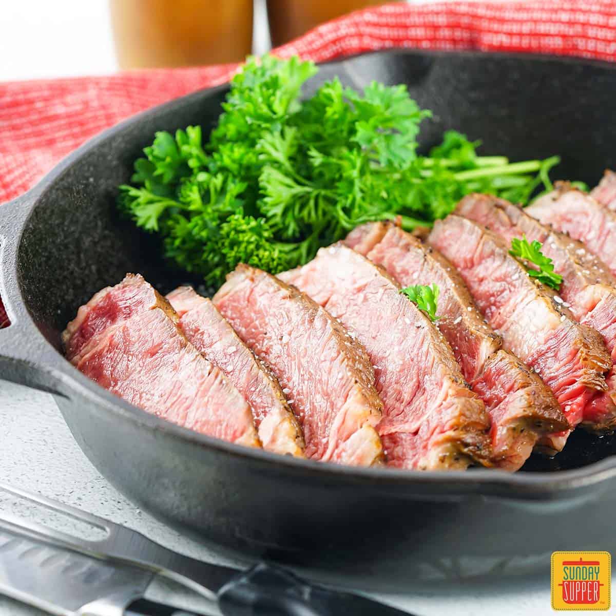 slices of sous vide ribeye steak next to fresh herbs in a cast iron pan