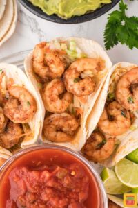 three shrimp tacos using air fryer shrimp next to a bowl of salsa and lime wedges
