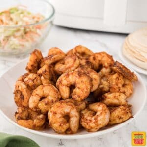 air fryer shrimp on a plate next to a bowl of coleslaw and a plate of tortillas