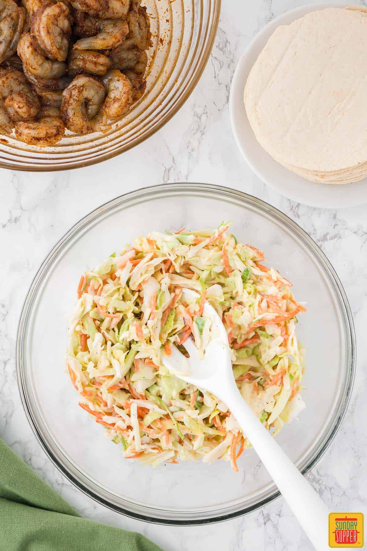 mixing coleslaw for shrimp tacos recipe in a bowl with a white slotted spoon