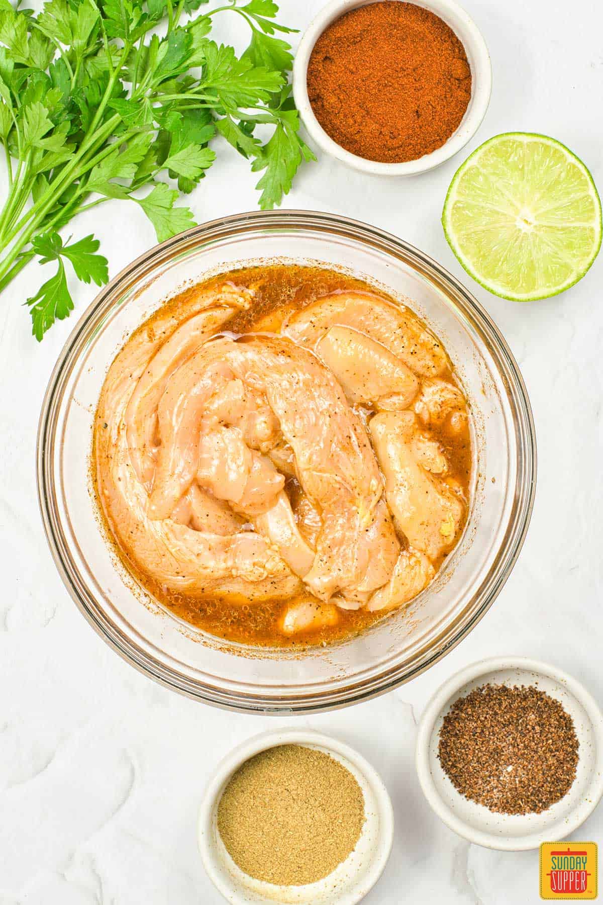 the chicken in a marinade in a glass bowl with extra spices
