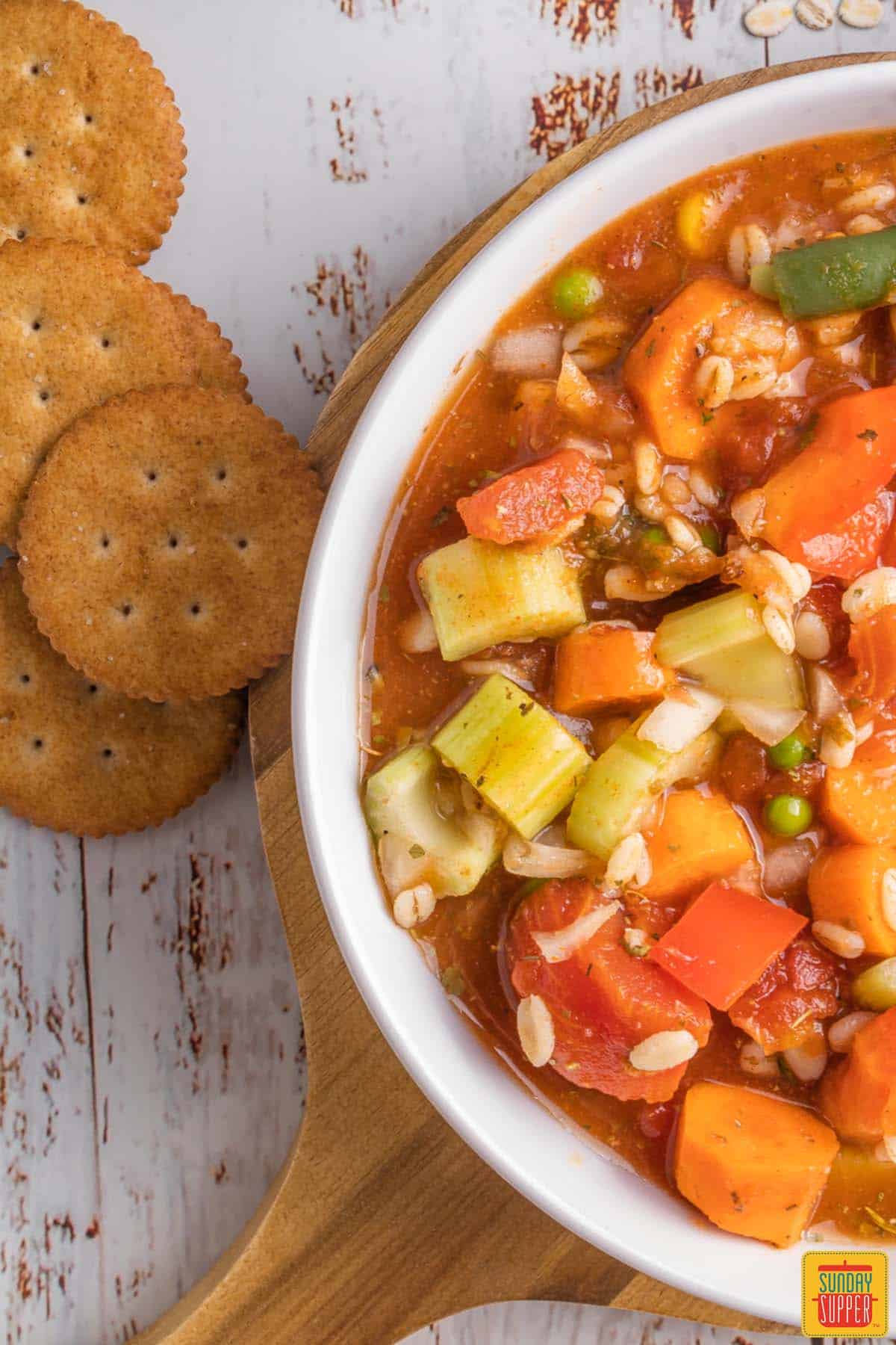 crockpot vegetable soup in a white bowl next to ritz crackers