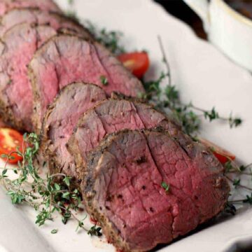 sliced whole beef tenderloin on a white platter with herbs