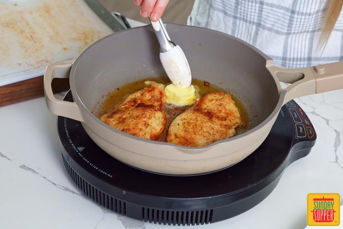 adding butter to a skillet with chicken