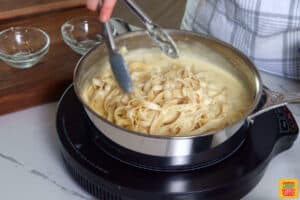 adding fettuccine noodles to Alfredo sauce in a skillet