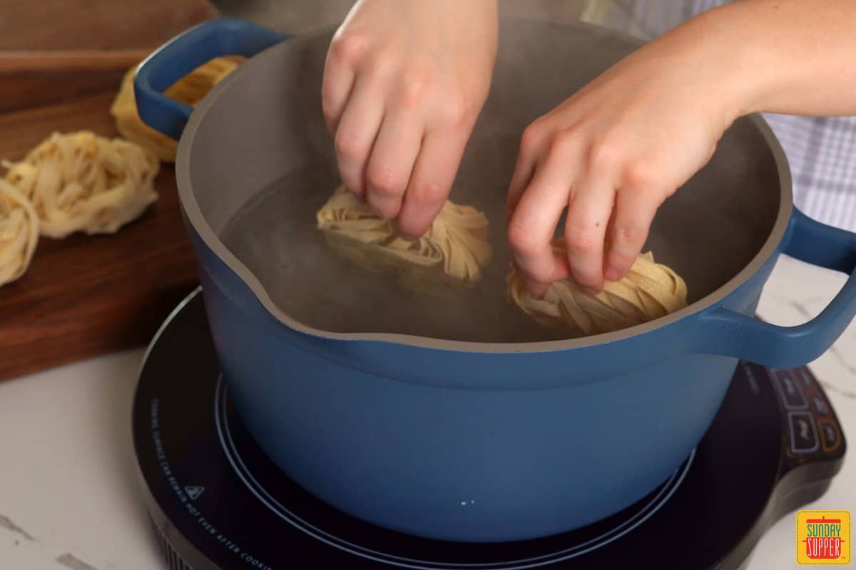 adding fettuccine noodles to boiling water