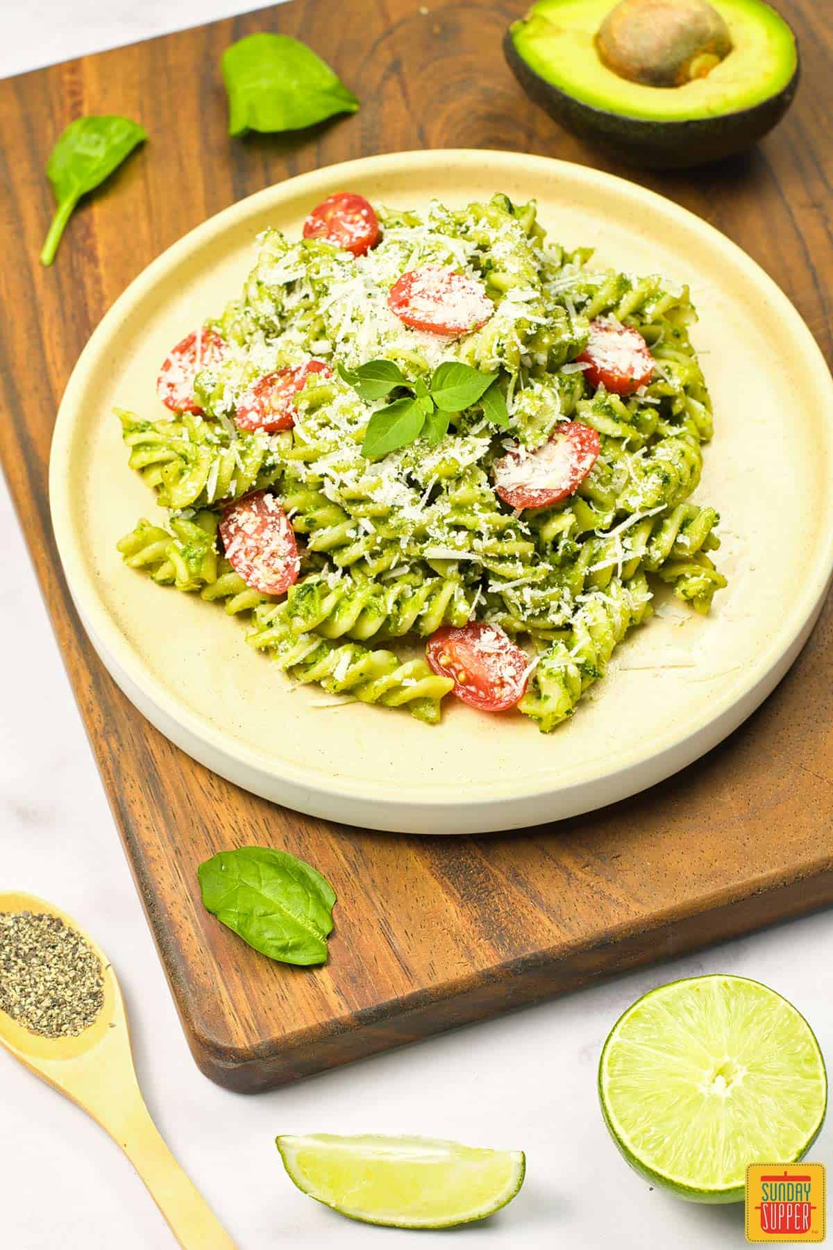 a completed plate of avocado pasta with basil, tomato and parmesan garnish