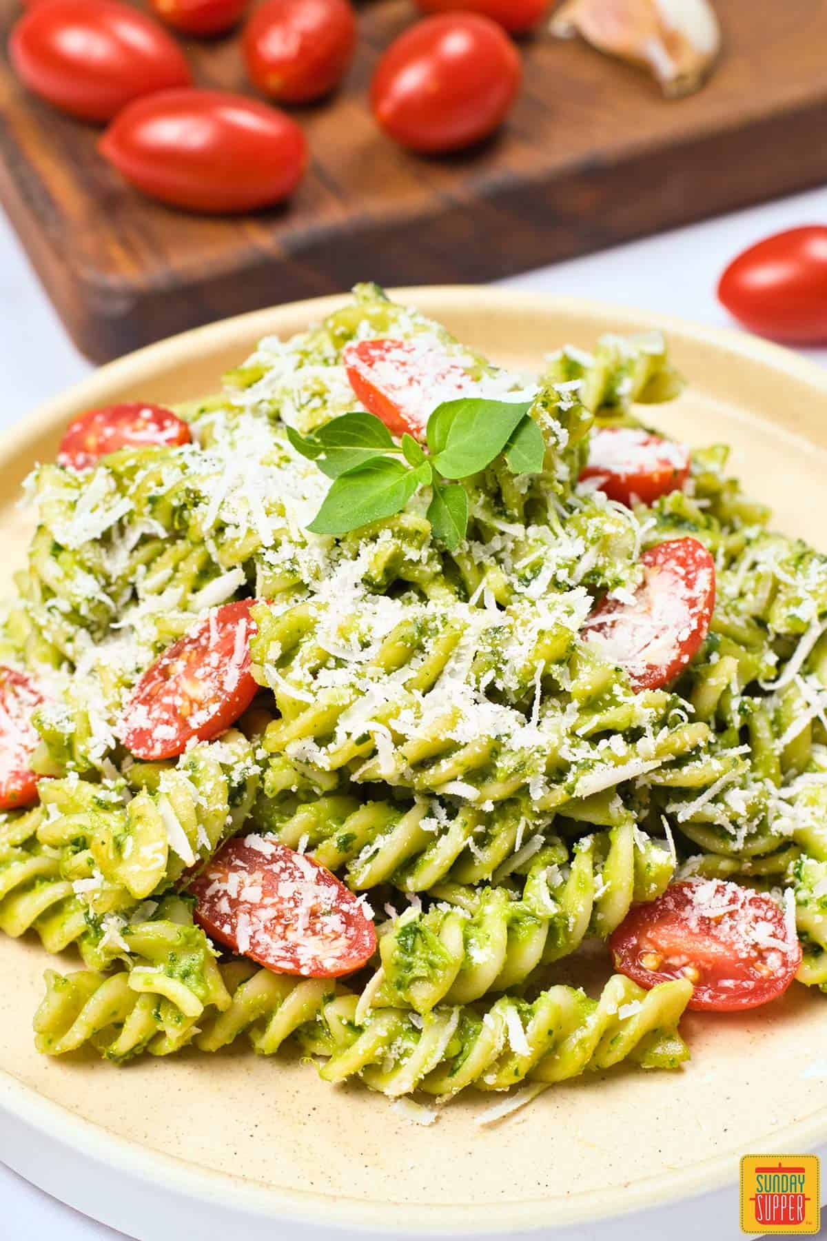 a dinner plate filled with creamy avocado pasta with tomatoes in the background