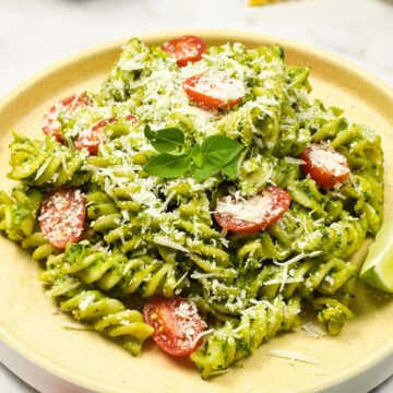 a plate of avocado pasta with a garnish of basil and parmesan