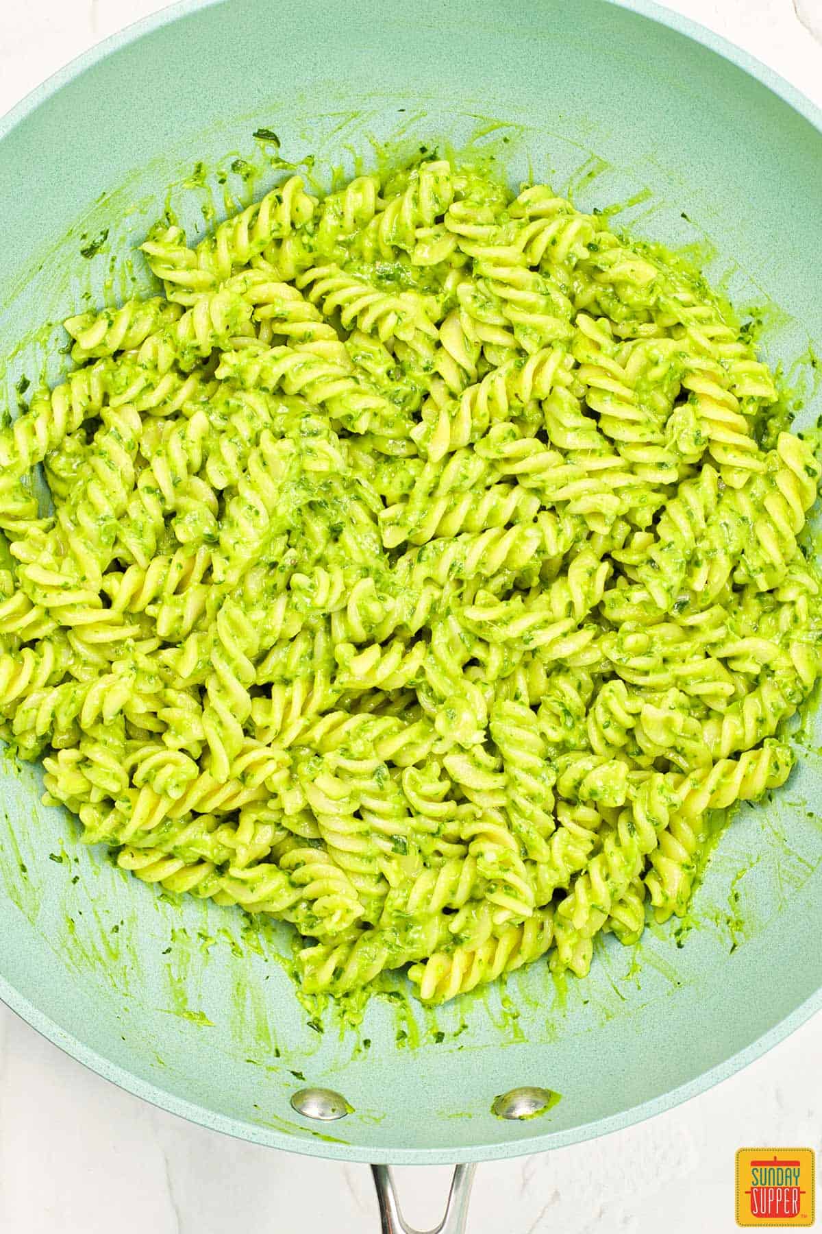 the pasta added into the avocado pasta sauce in a pan
