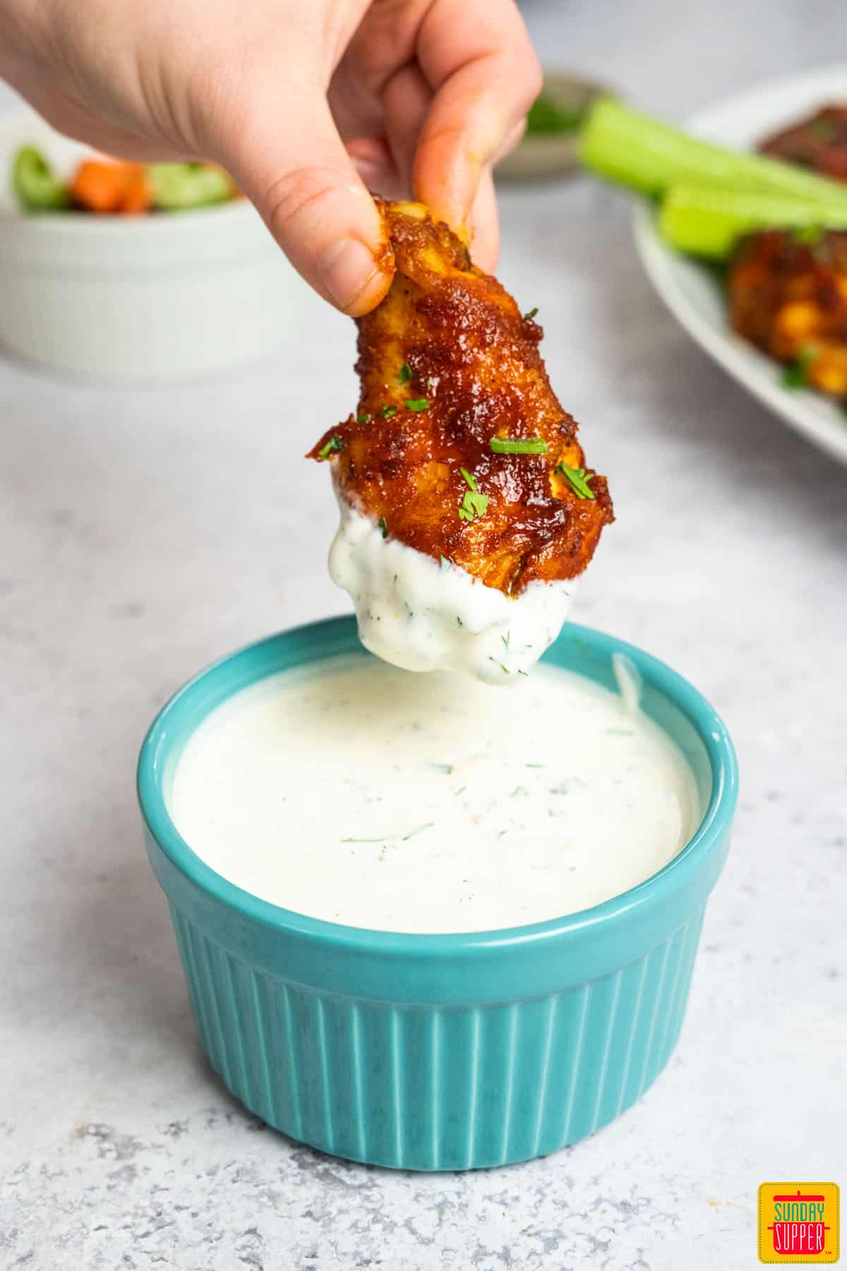 chicken wing dipping into ranch dressing in a blue dish