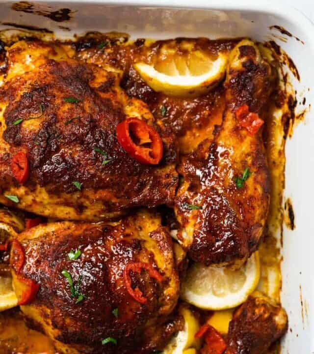 peri peri chicken up close in a roasting dish with lemon wedges