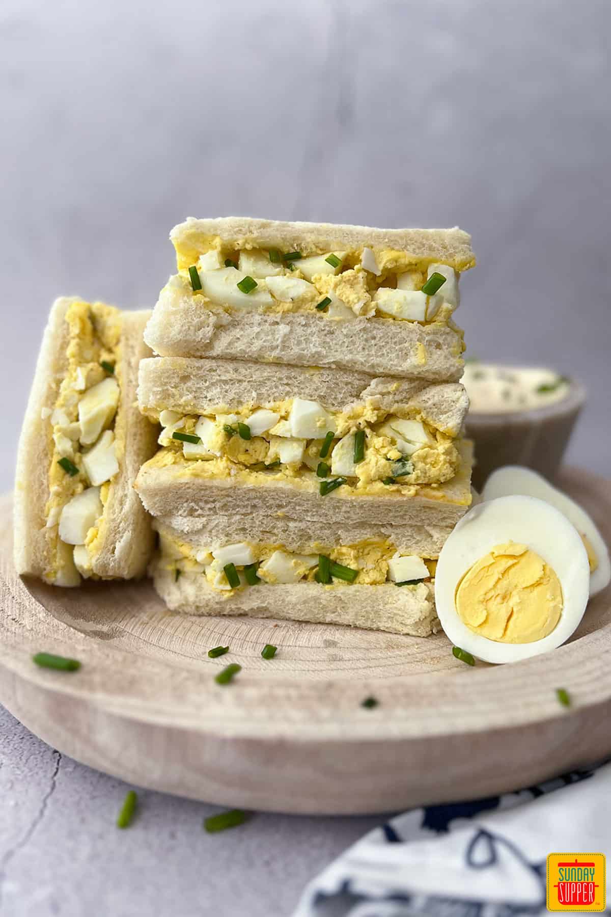 egg sandwiches stacked up on a wood plate