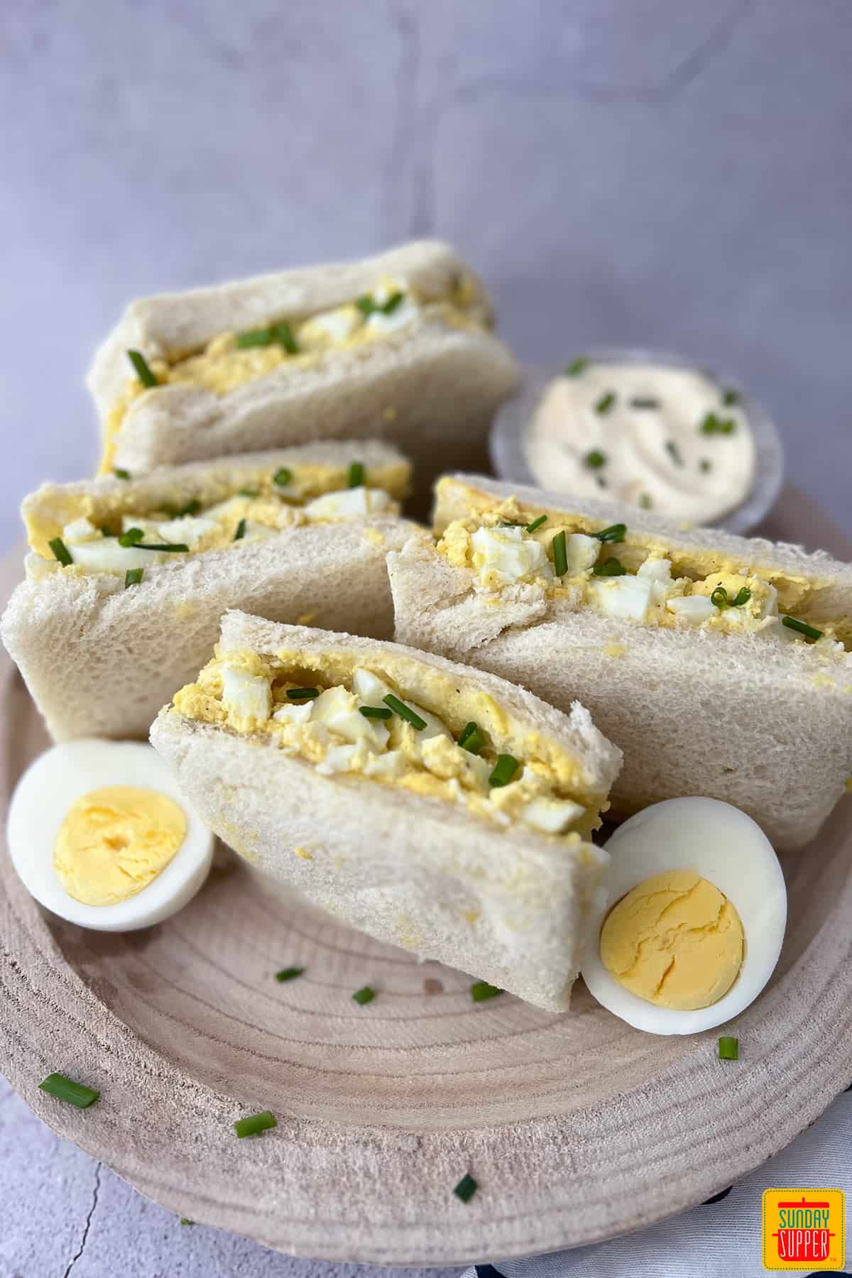 egg sandwiches on a wood cutting board with slices of hard-boiled eggs next to them