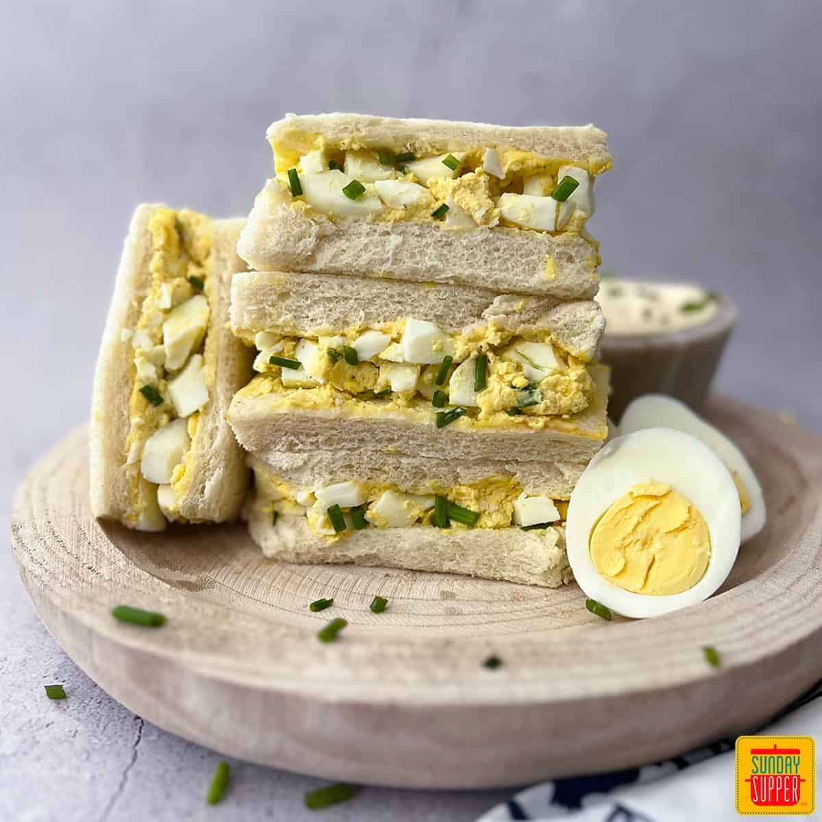 egg sandwiches stacked high on a wood plate