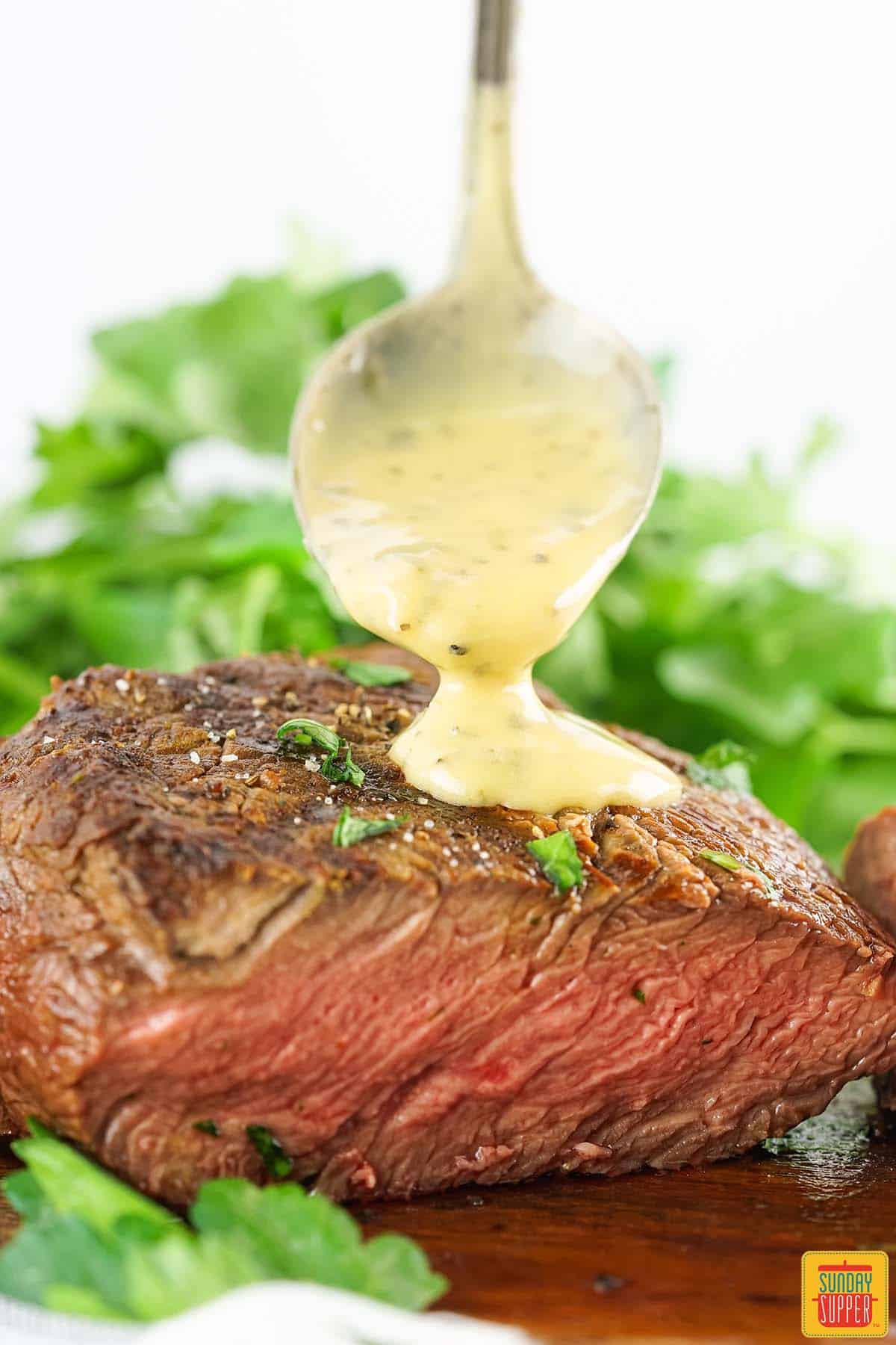 bearnaise sauce being spooned on to a grilled filet mignon