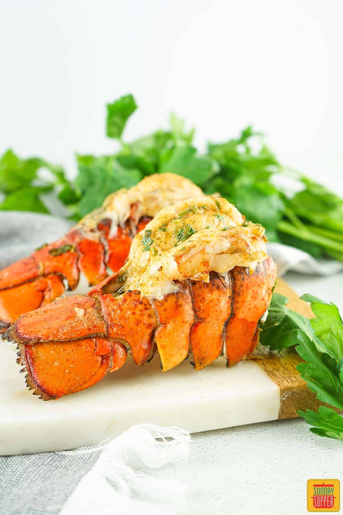 two grilled lobster tails on a serving board with parsley
