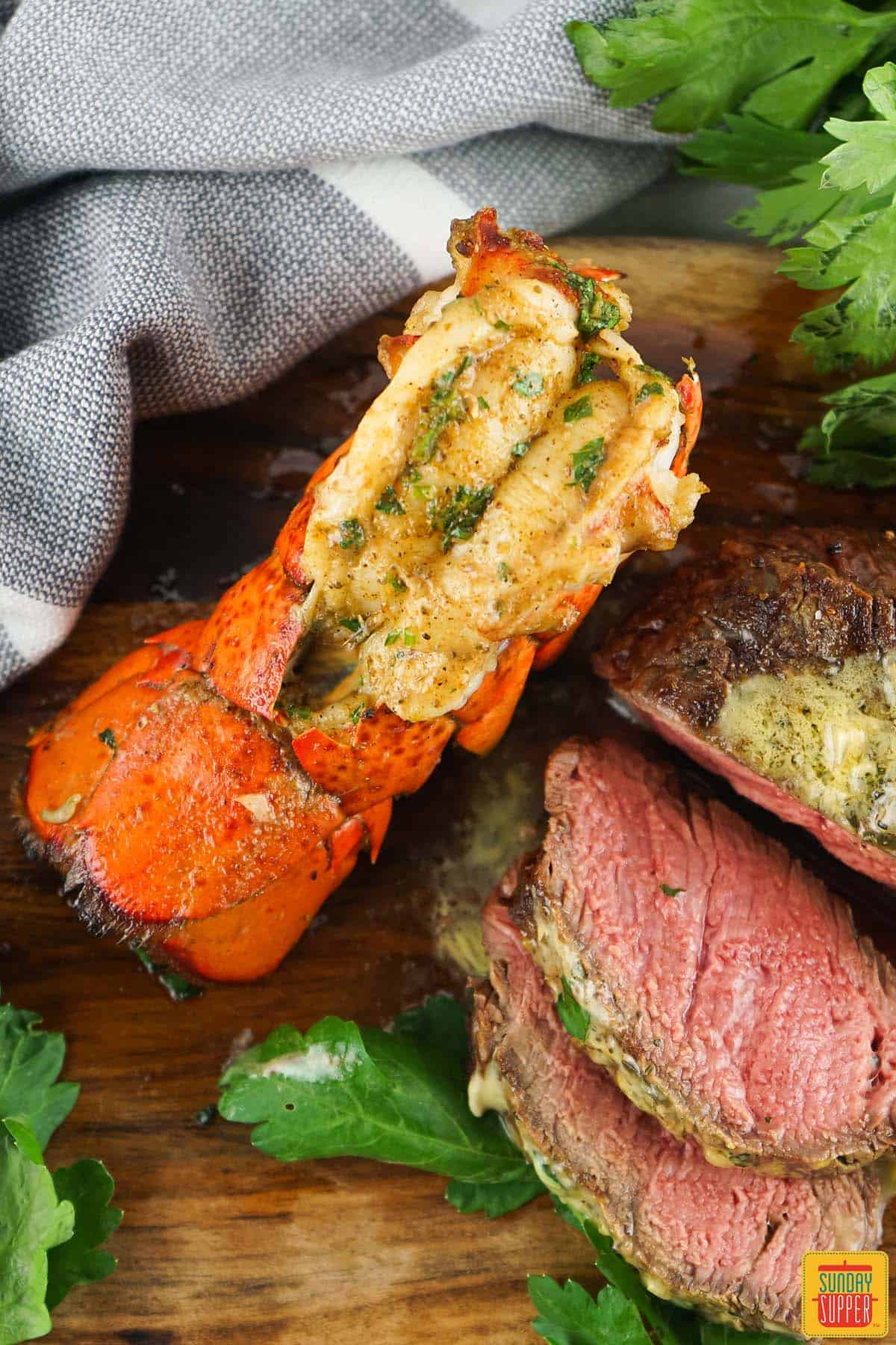 grilled lobster tail with grilled filet mignon on a cutting board with herbs