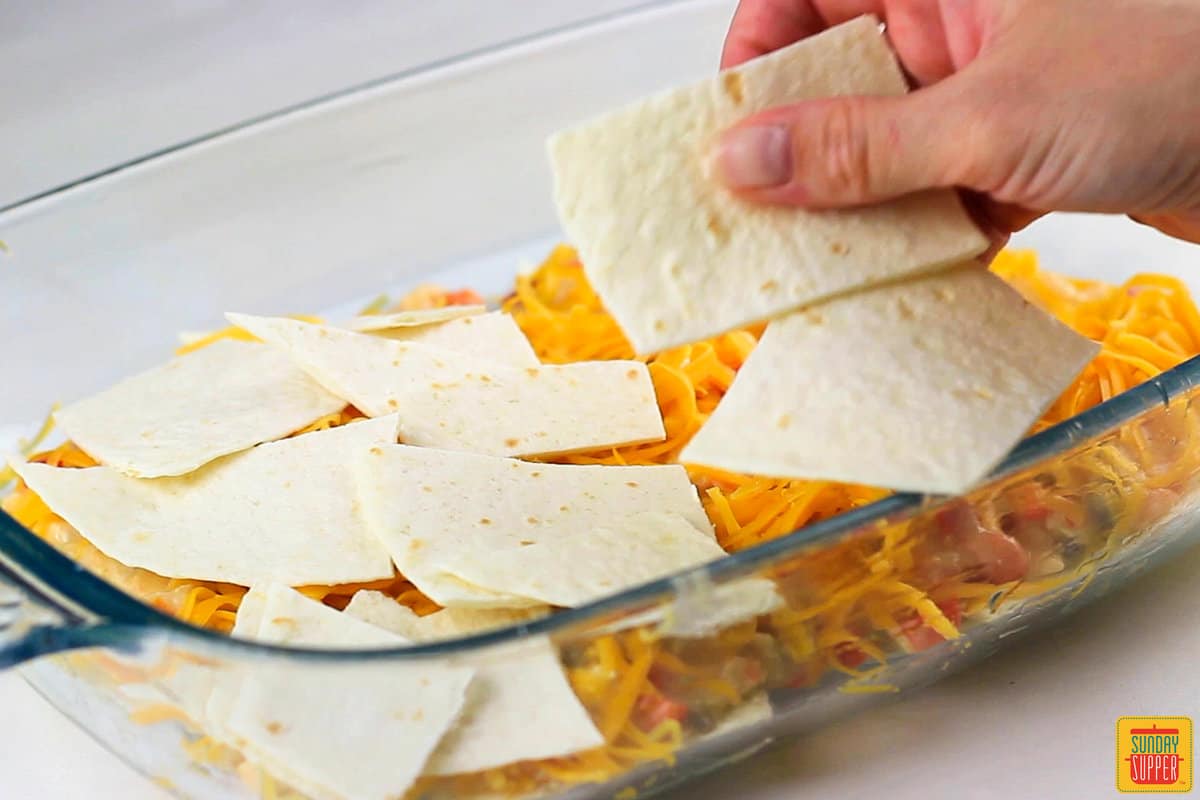 tortilla pieces being layered into the casserole dish