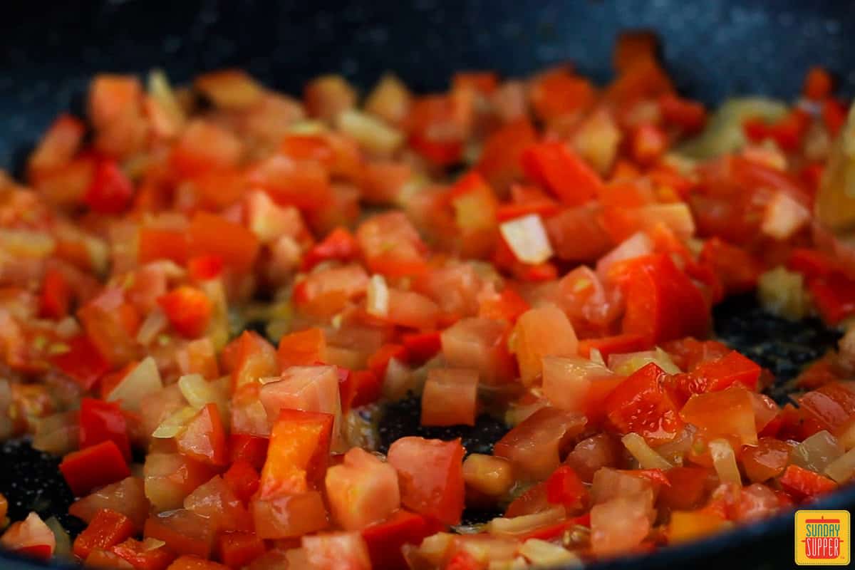 onions, tomatoes, and chilies being sauteed in a pan