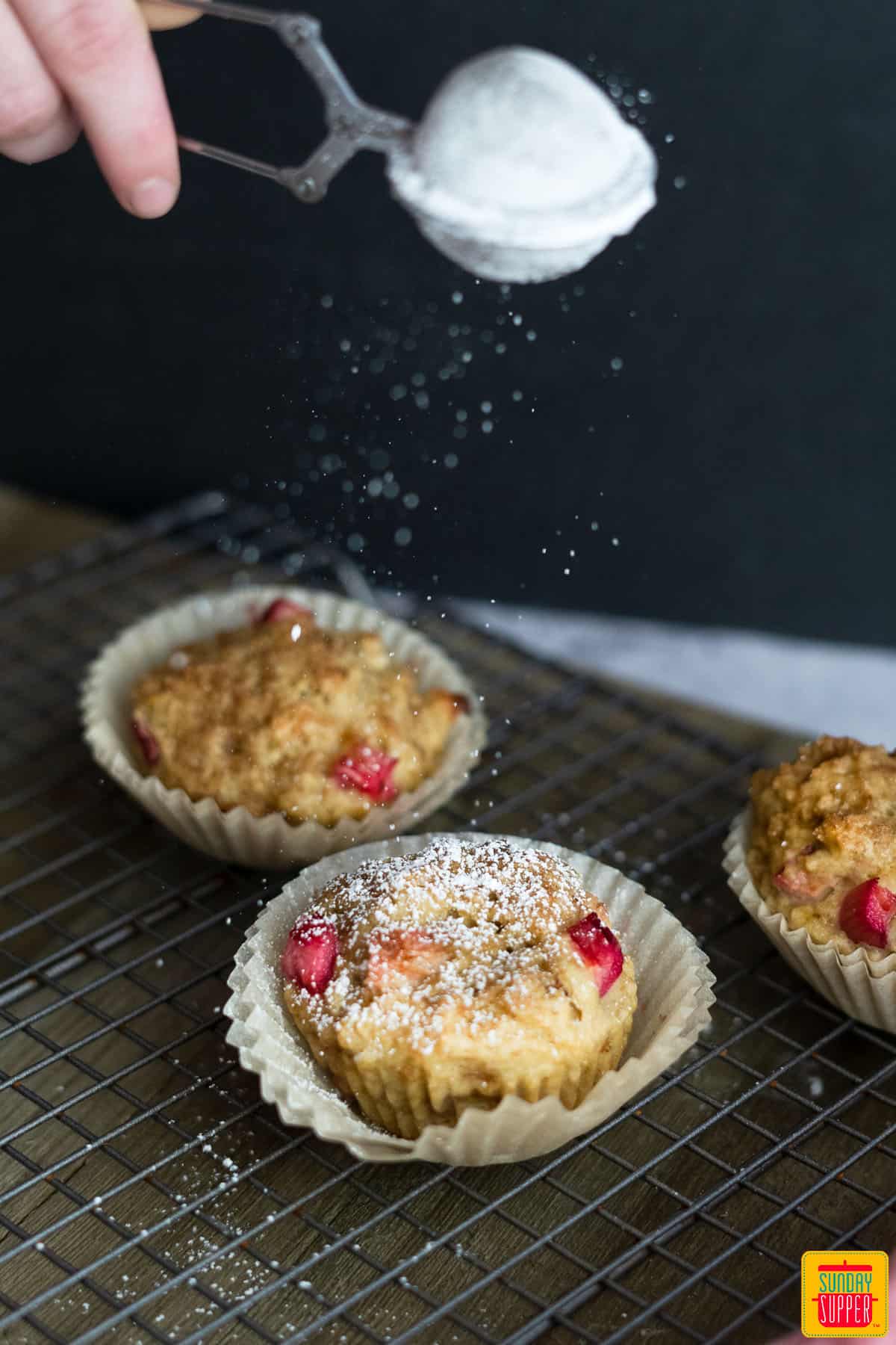 sprinkling powder sugar on rhubarb muffins