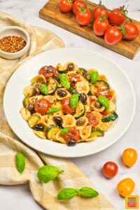 a white plate with summer pasta salad surrounded by tomatoes
