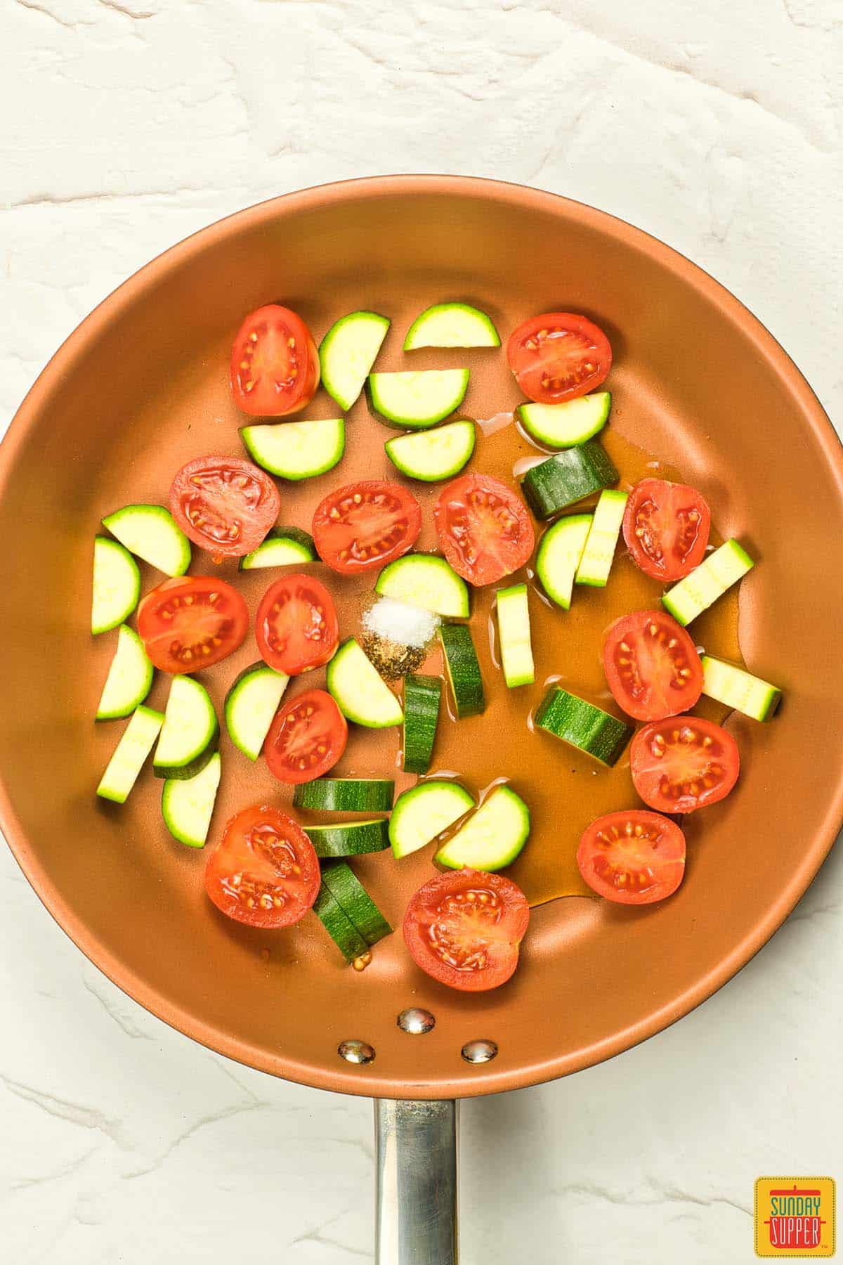 sliced tomatoes and zucchini in a pan with salt and pepper