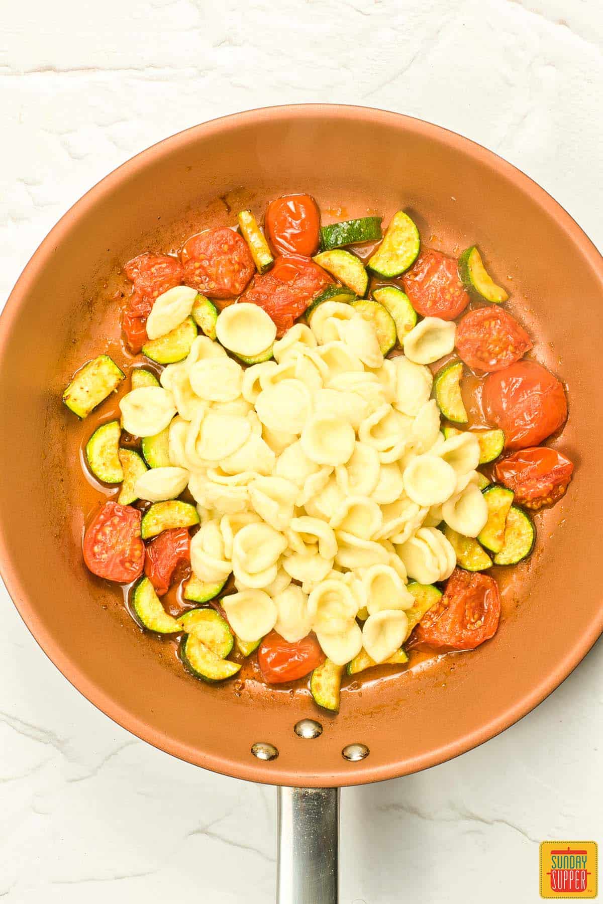 adding orecchiette pasta to pan of zucchini and tomatoes