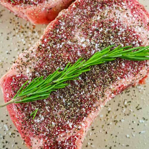 a steak seasoned with salt, pepper, and a rosemary sprig