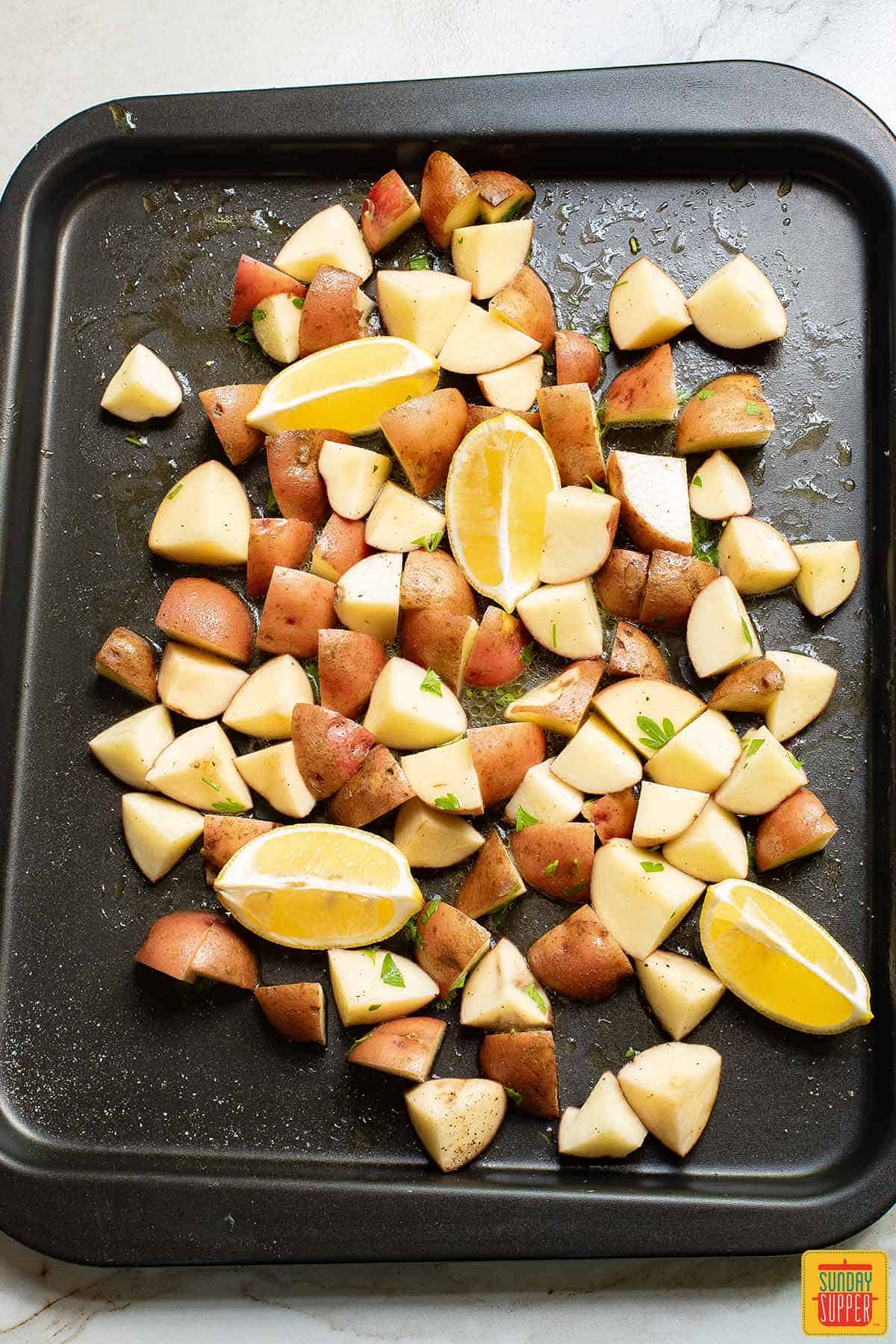lemons and potatoes with seasonings on a pan before cooking
