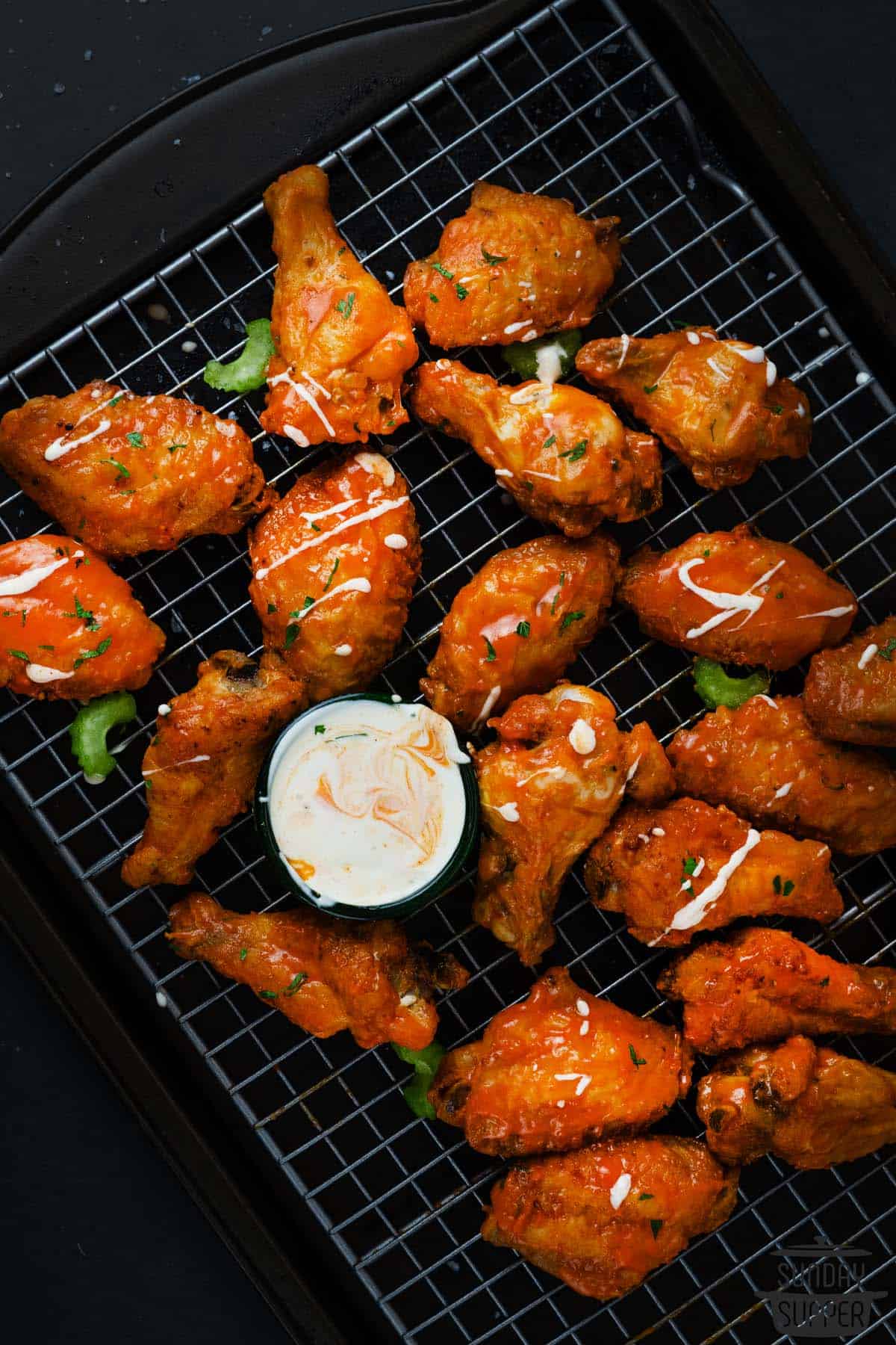 buffalo wings next to blue cheese dip on a baking tray drizzled with dressing