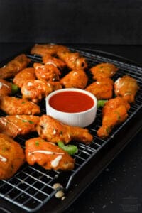 buffalo wings on a baking tray with buffalo sauce in a dipping bowl