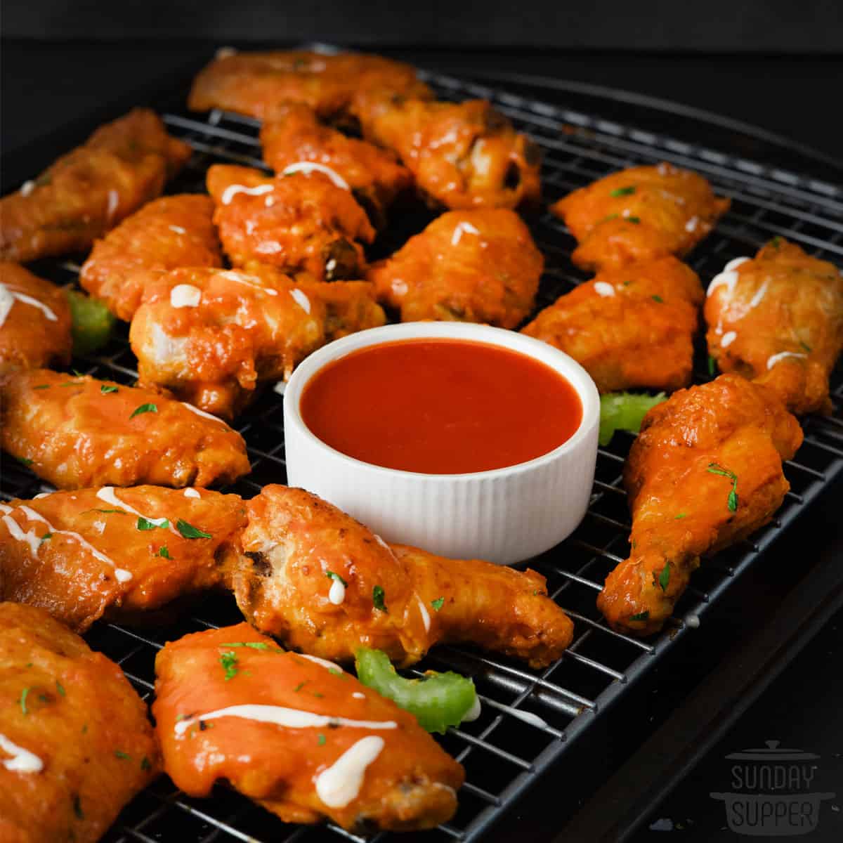 buffalo wings on a cooling rack over a baking tray with buffalo sauce in a cup