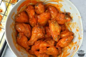 mixing chicken wings with buffalo sauce in a bowl