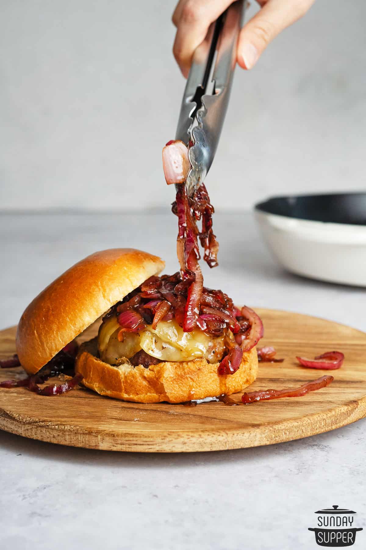 adding caramelized onions to a burger with tongs