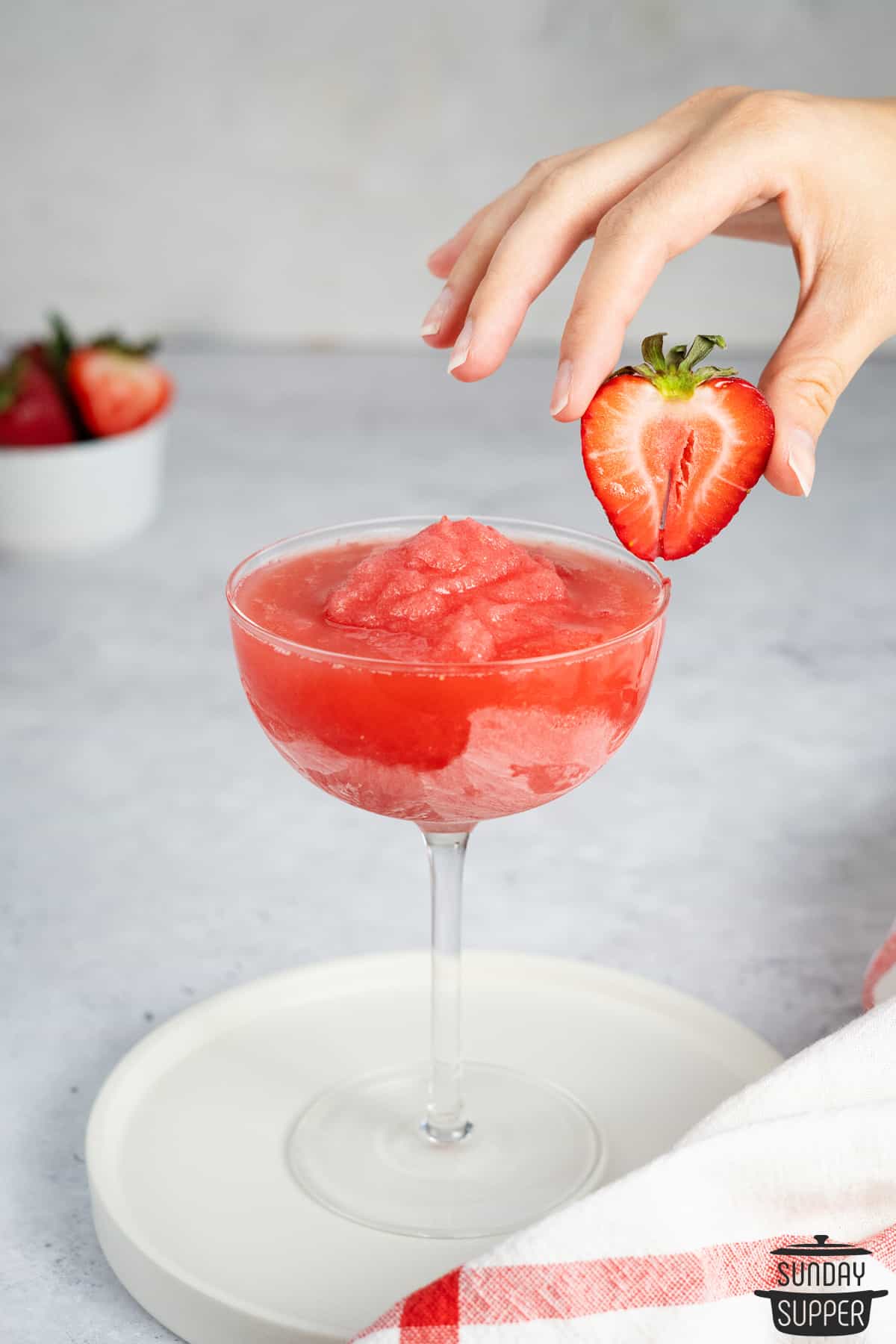 taking a strawberry slice off of the rim of a glass of frose
