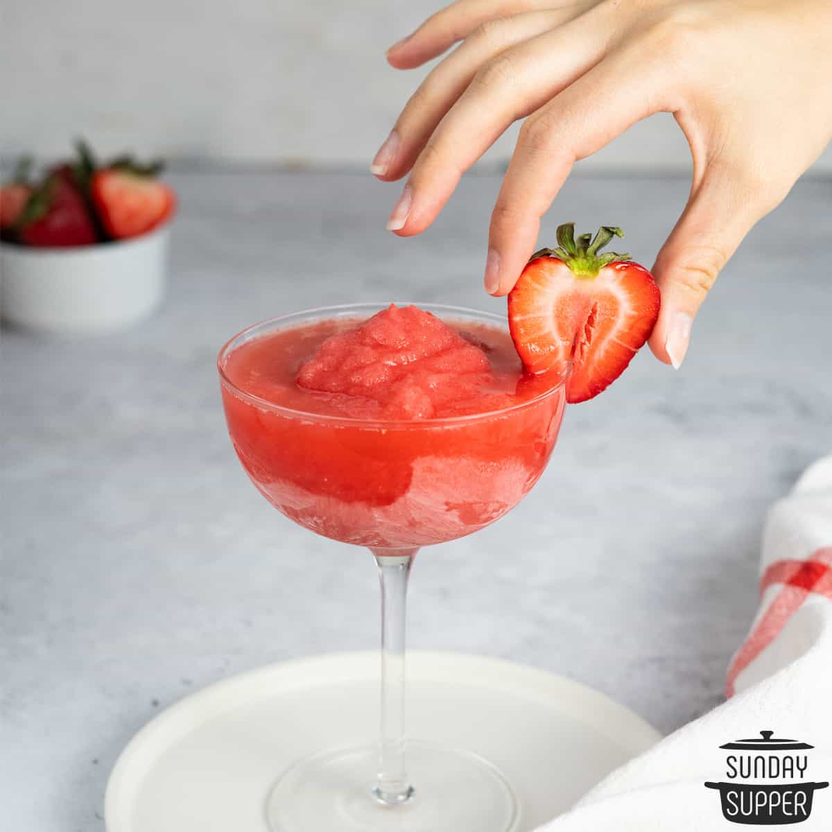 placing a strawberry on the rim of a glass of strawberry frose