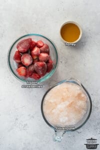 frozen strawberries, honey, and frozen rose in two bowls and a measuring cup