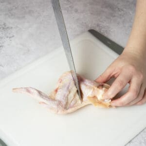 Slicing through the first ridge of a chicken wing using a sharp knife on a cutting board