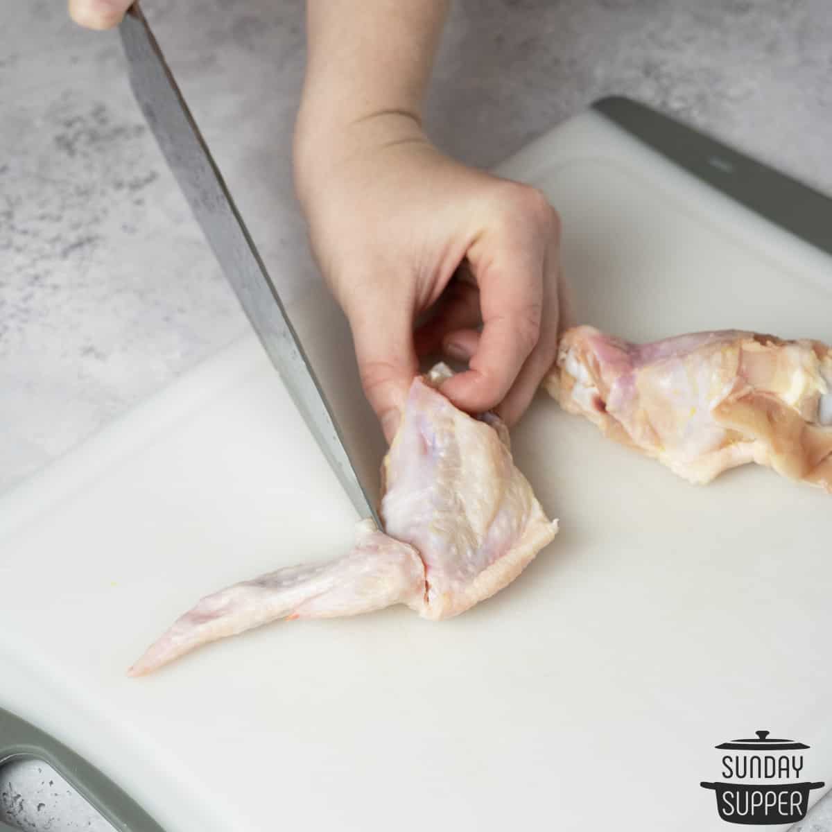 Slicing the wing tip off of a chicken wing using a sharp knife