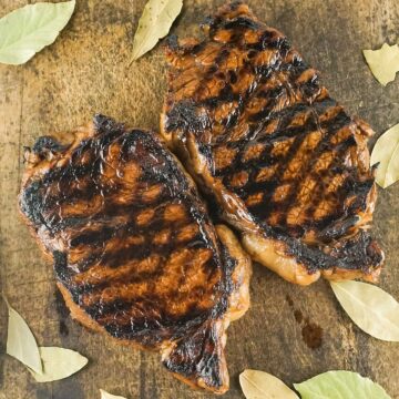 two grilled NY steaks on a cutting board with bay leaves
