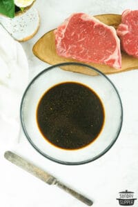 mixed asian marinade in a bowl next to raw strip steaks