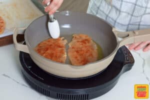 using tongs to add chicken to a pan with olive oil