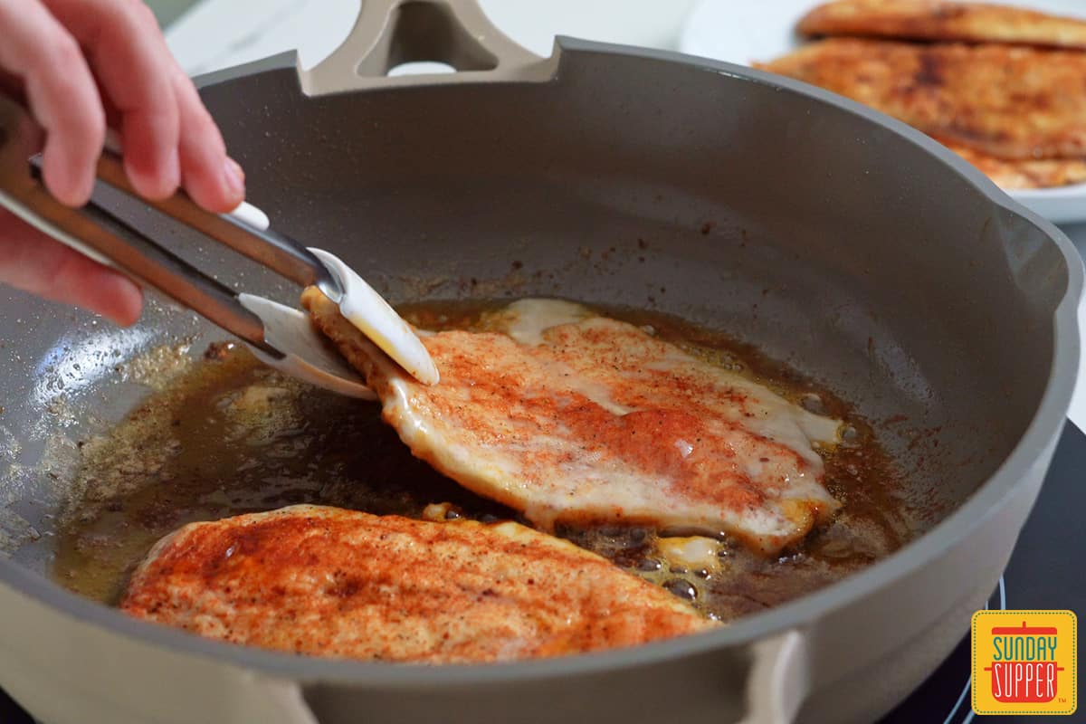 flipping chicken in the pan with tongs