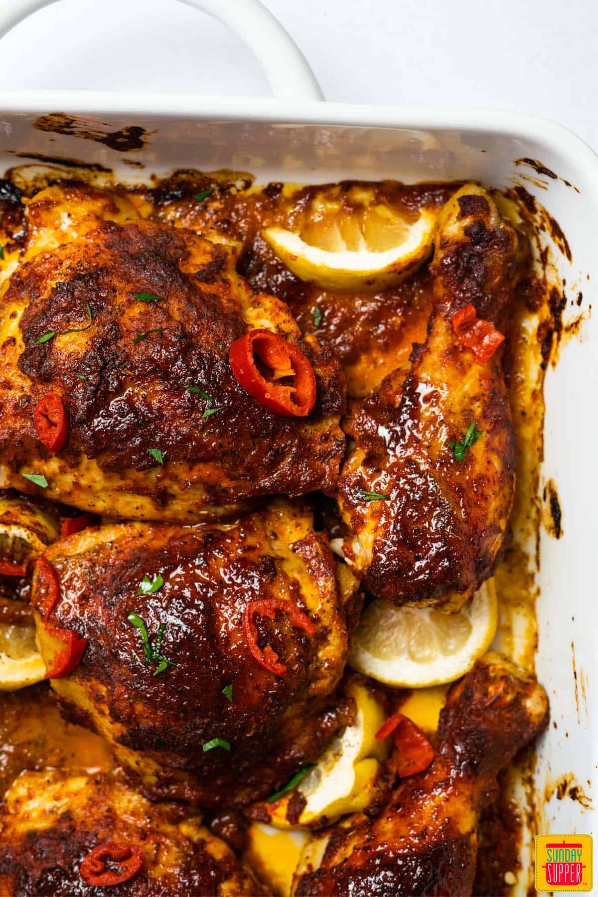 peri peri chicken in a white roasting pan with lemon wedges and chili slices