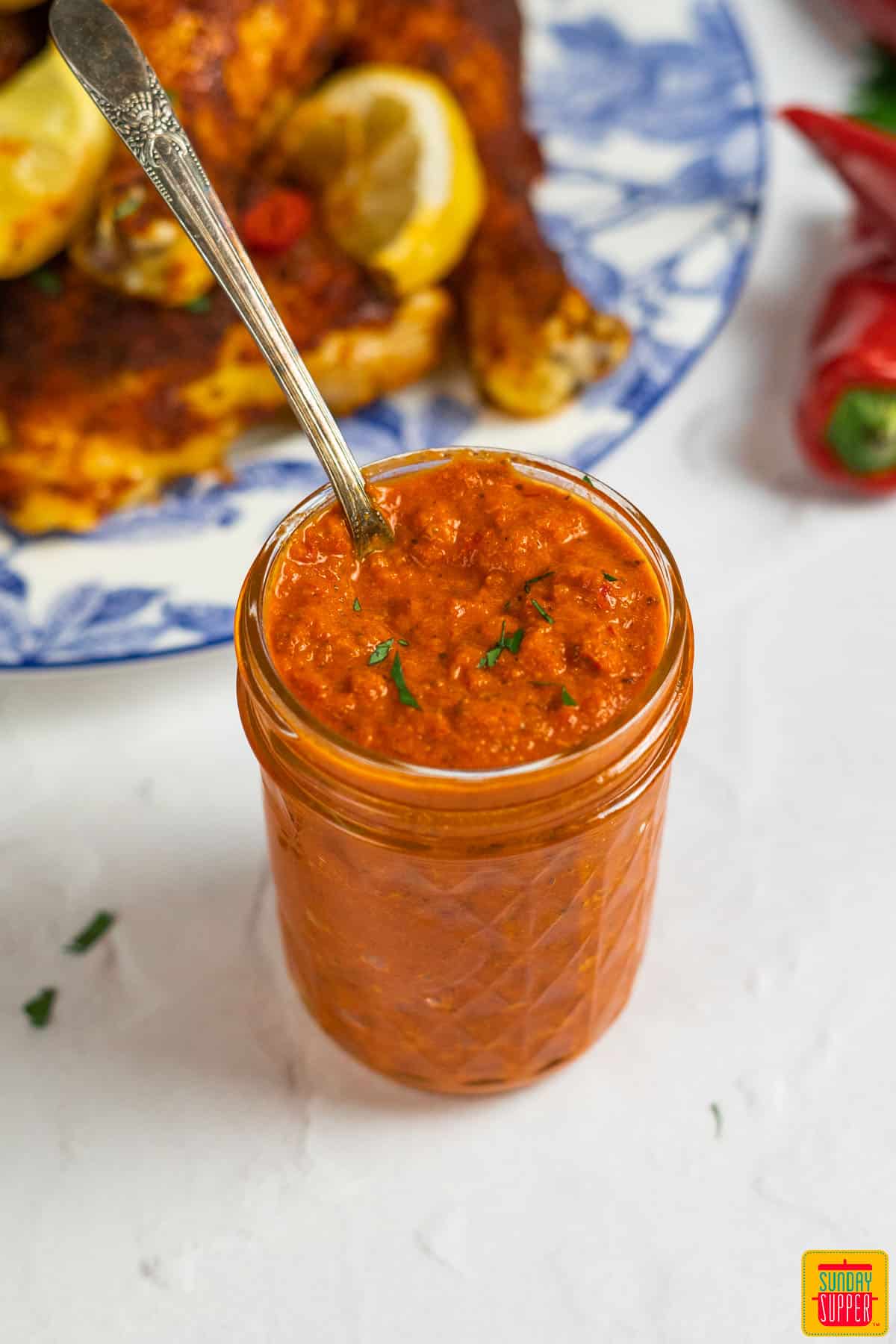 peri peri sauce in a glass jar with a spoon beside a plate of chicken