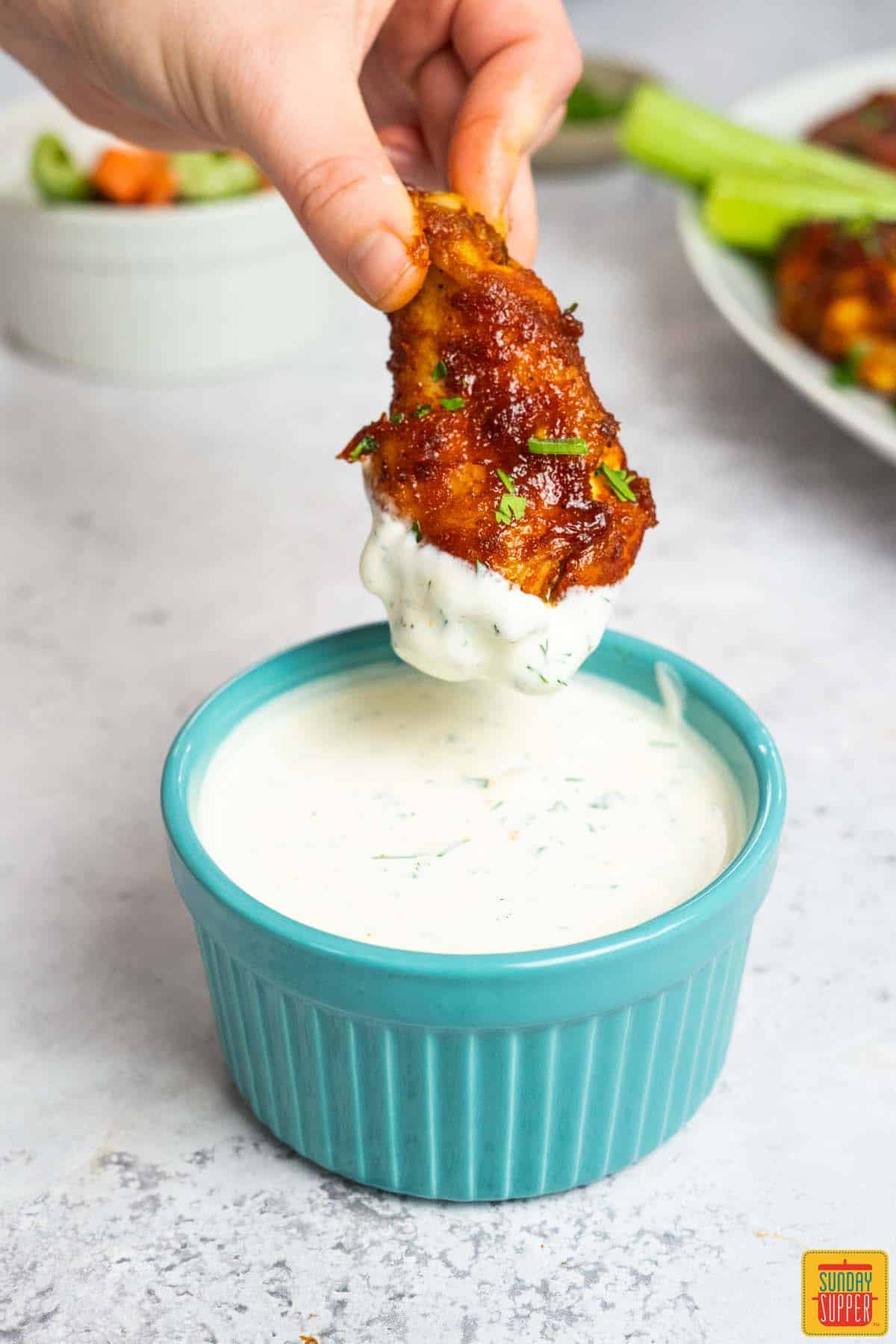 ranch dressing in a blue dish with chicken wing dipping inside