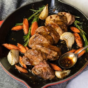 pork tenderloin sliced in a pan with garlic, carrots, and herbs