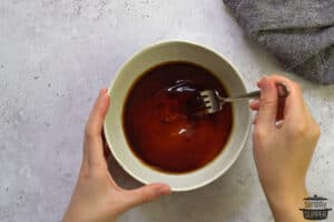 stirring honey garlic sauce in a white bowl with a fork